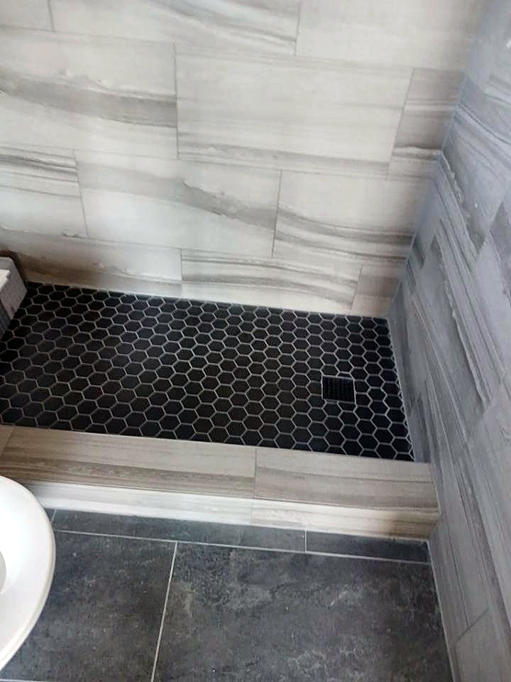 New shower with large white wall tile and a black hex-tile floor