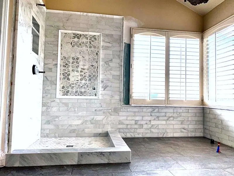 Finished bathroom remodel with a marble-tile shower, a patterned accent panel and white shutters