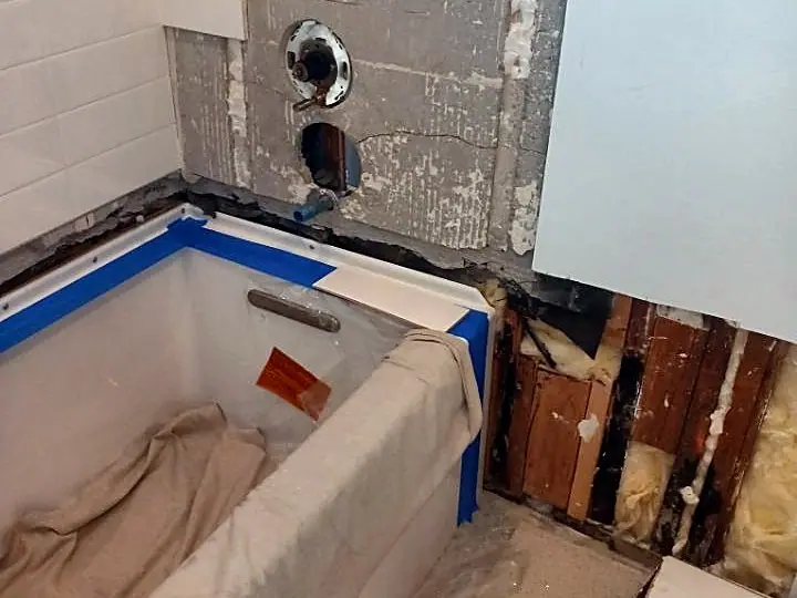 Tub area with the wall opened up, showing old framing and plumbing behind the tile