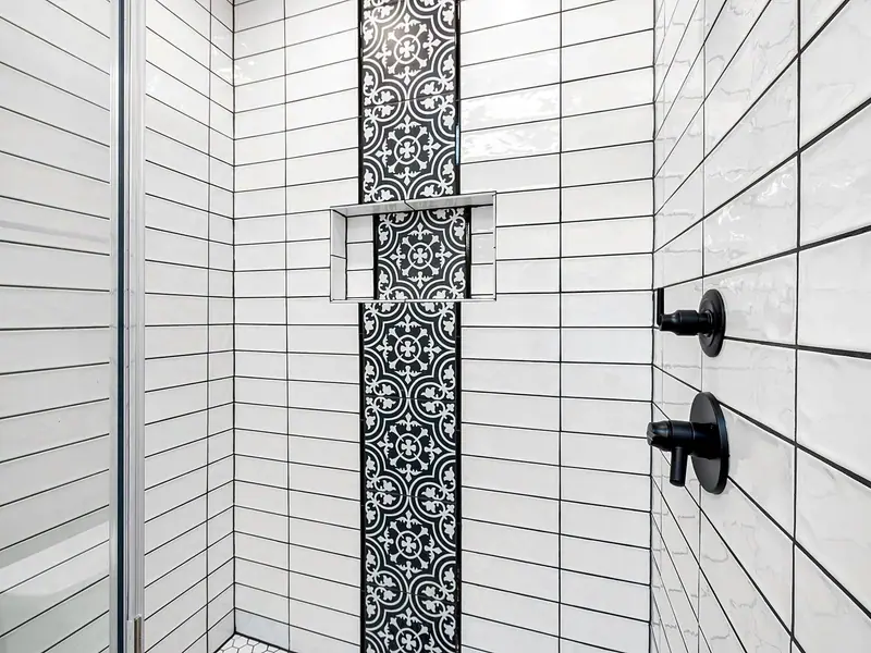 Shower wall in long white tile with a black-and-white patterned stripe and a recessed niche