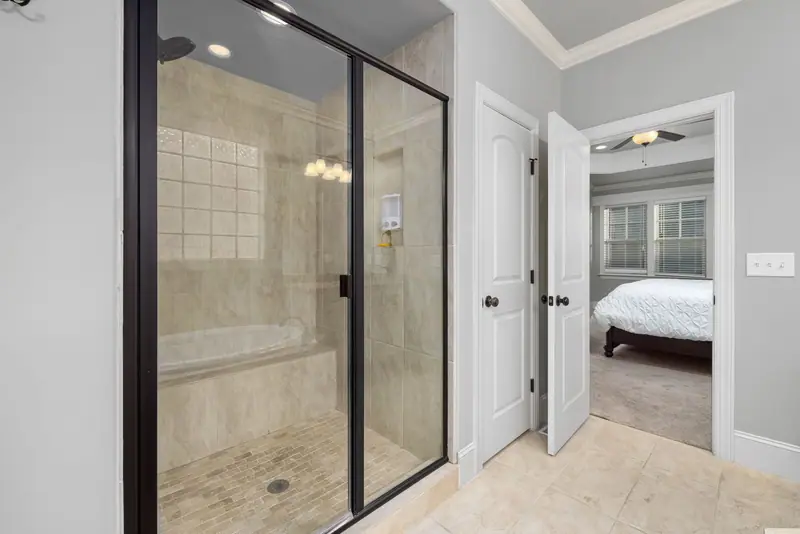 Shower with a framed glass door with black trim, a tiled bench and a tile floor, next to a bedroom door