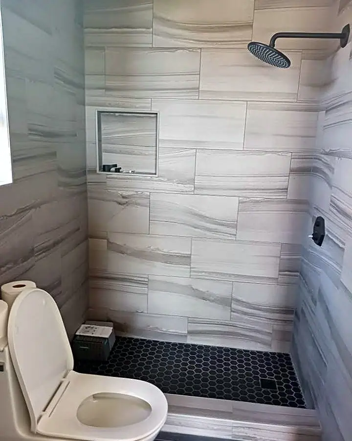 Tiled walk-in shower with a recessed niche in the back wall, a rain shower head and a black hexagon tile floor