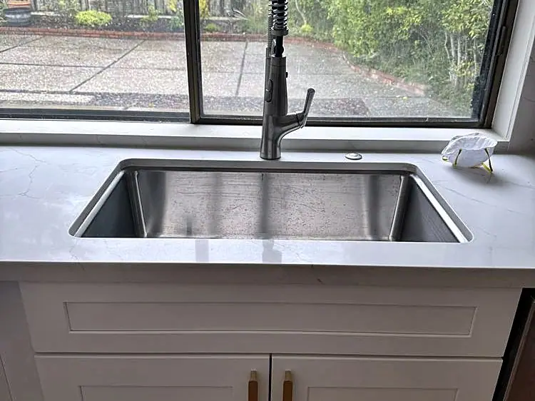 Stainless undermount sink and pull-down faucet set in a white quartz counter under a window
