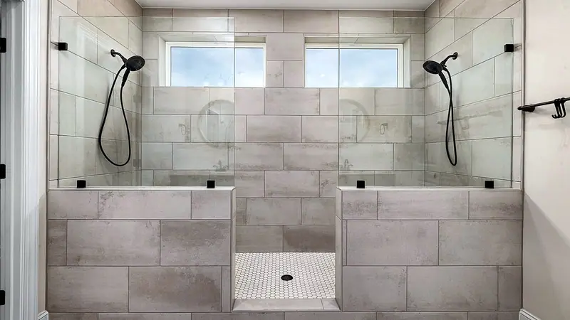 Wide walk-in shower with gray tile, a long bench, two shower heads and frameless glass