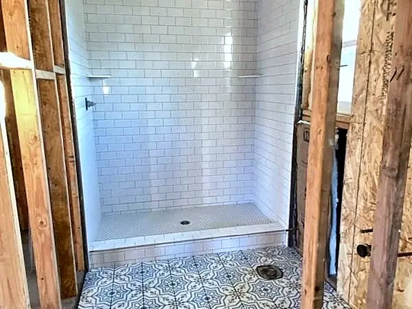 Bathroom wall opened to the studs while a new tiled shower goes in, with a patterned tile floor