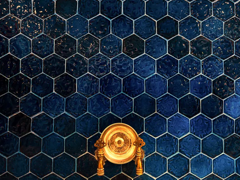 Blue hexagon tile on a shower wall around a brass valve trim