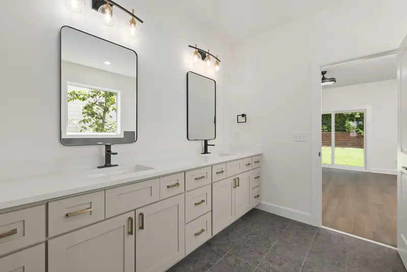 Long white double vanity with black-framed mirrors and a black three-light bar fixture above each mirror