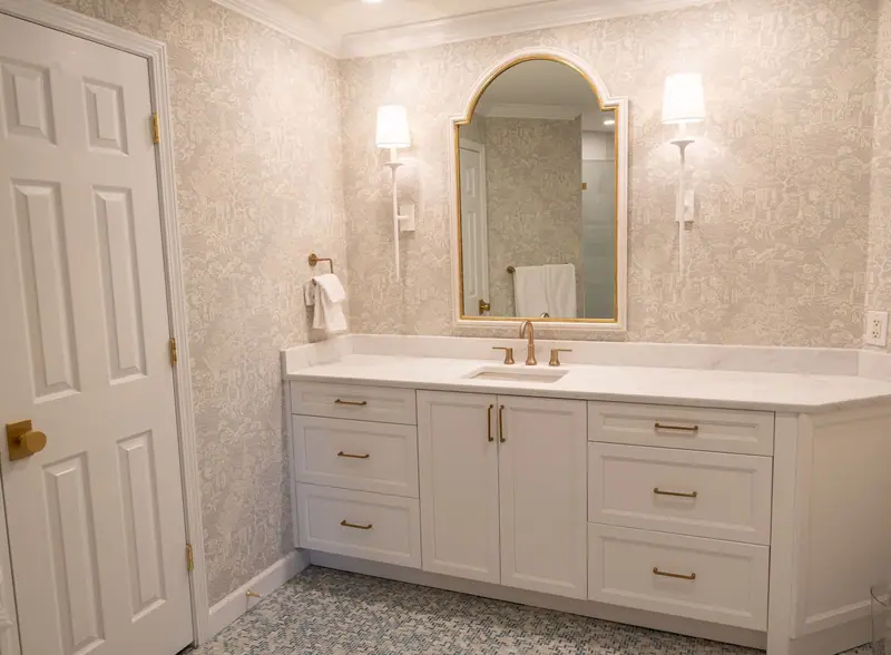 White bathroom vanity with a stone top, an arched mirror and a wall sconce on each side