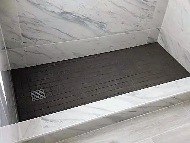 Finished walk-in shower with marble-look wall tile, a dark tile floor and a low tiled curb, before the glass goes in