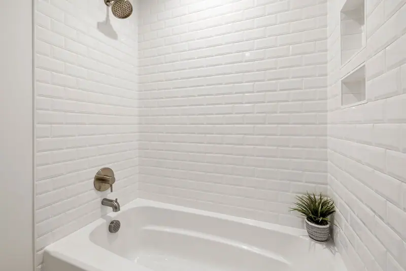 Alcove tub-shower combo with white beveled subway tile, two recessed wall niches and a brushed-metal shower valve